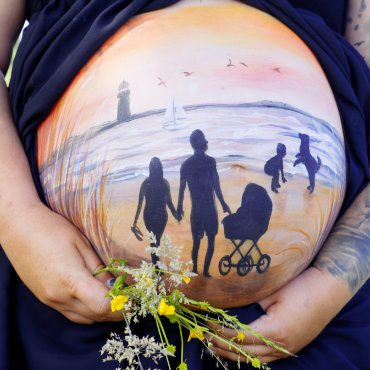 Bemalung auf Schwangerschaftsbauch mit einer Familie am Strand