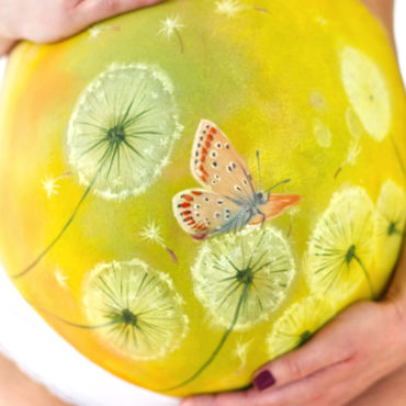 Bemalung auf Schwangerschaftsbauch mit einer Pusteblume mit Bläuling